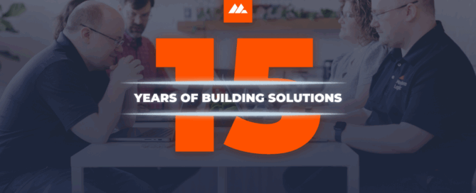 Modern Logic team gathered around a table with the number 15 in bold orange and the words “Years of Building Solutions” across the center, celebrating 15 years in business.