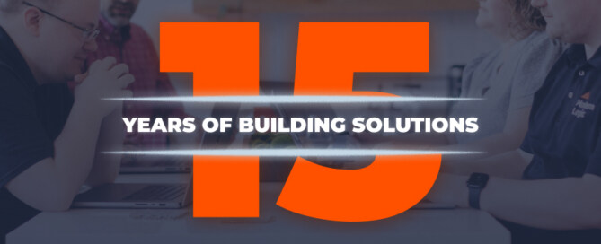Modern Logic team gathered around a table with the number 15 in bold orange and the words “Years of Building Solutions” across the center, celebrating 15 years in business.