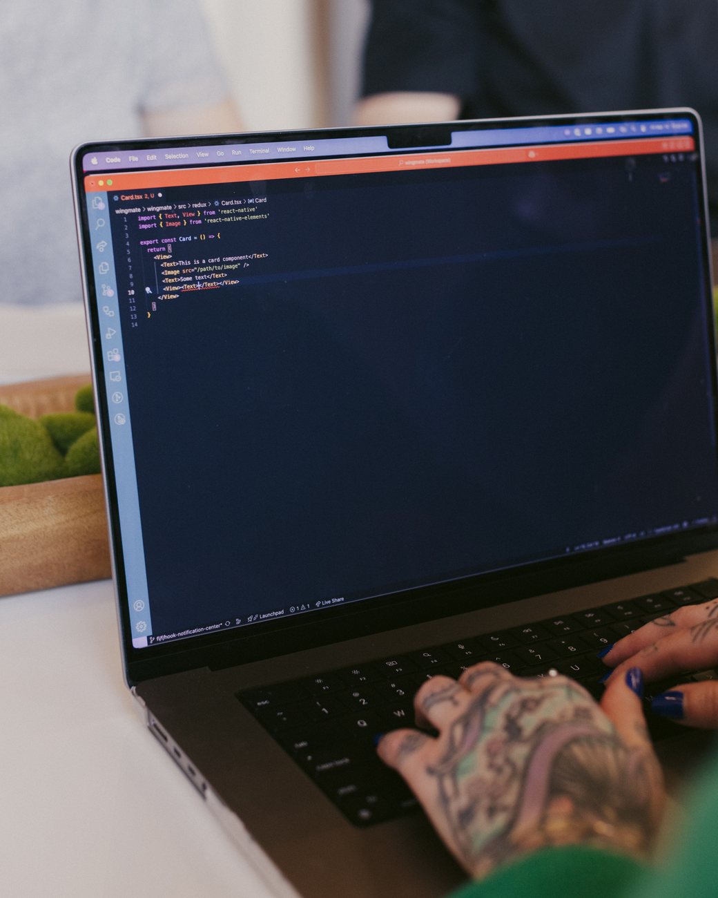 A developer’s tattooed hands typing on a laptop showing code in VS Code